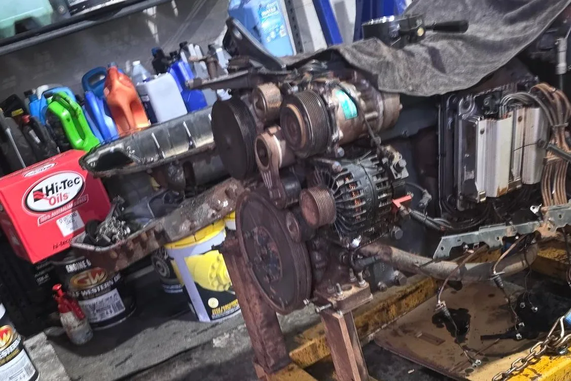 A diesel engine on a stand with the sump off, belts, pulleys and the alternator exposed