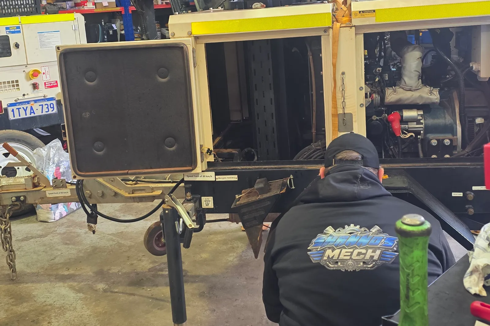 A Shanno&rsquo;s mechanic in a Shanno&rsquo;s Mech hoodie working under a lighting tower trailer in the workshop