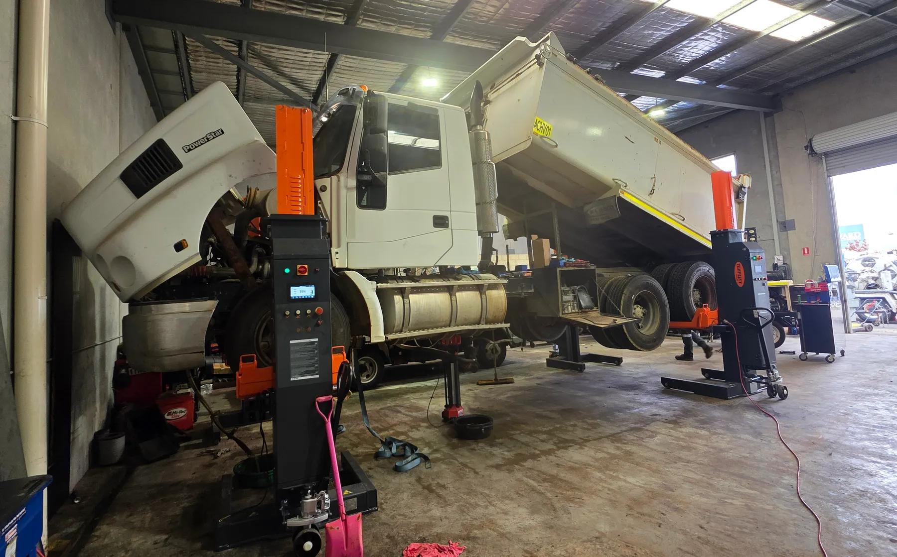 A white Iveco PowerStar tipper up on column lifts in the workshop with the cab tilted forward